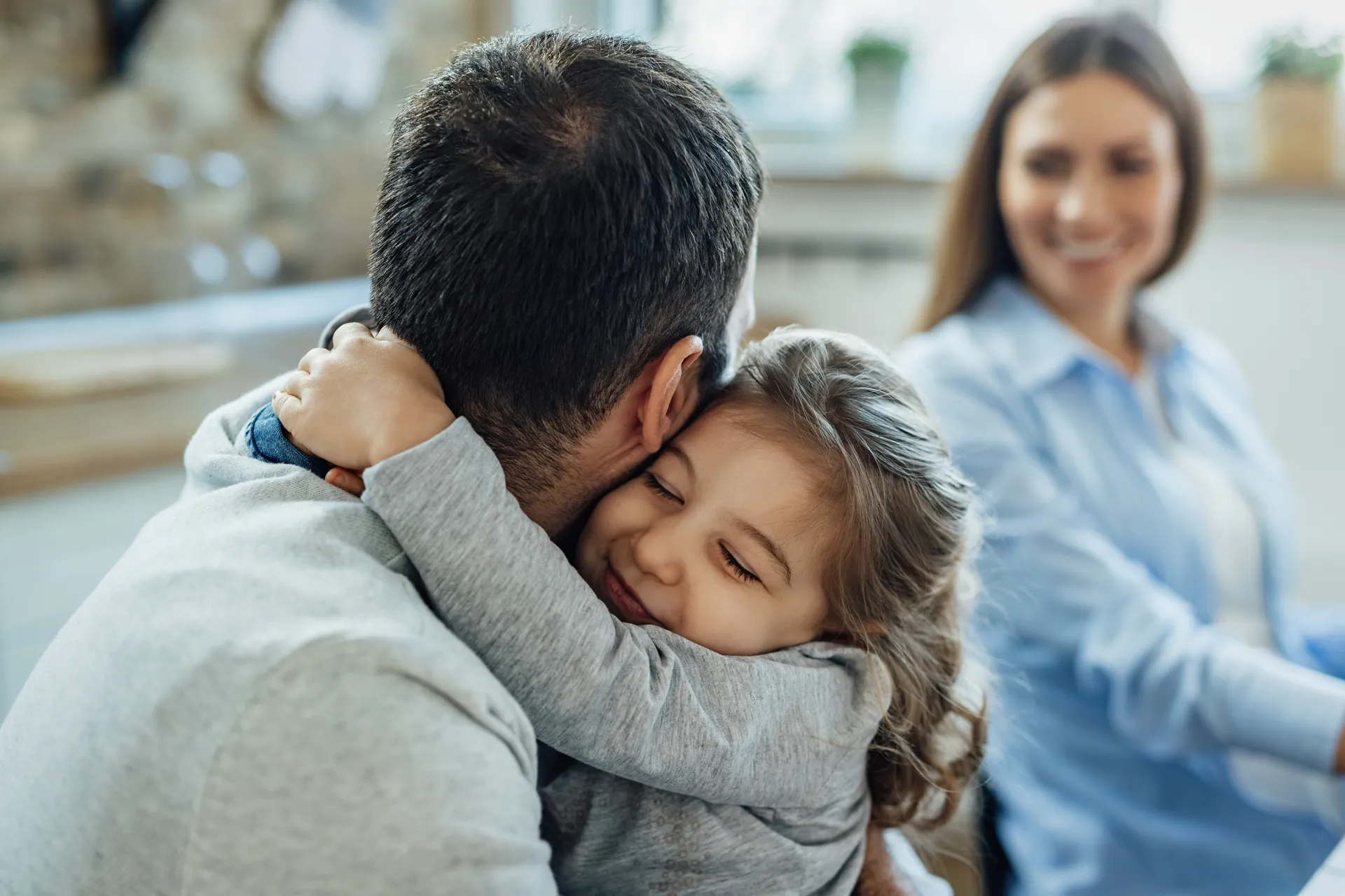 Bambina che abbraccia il papà con mamma sullo sfondo